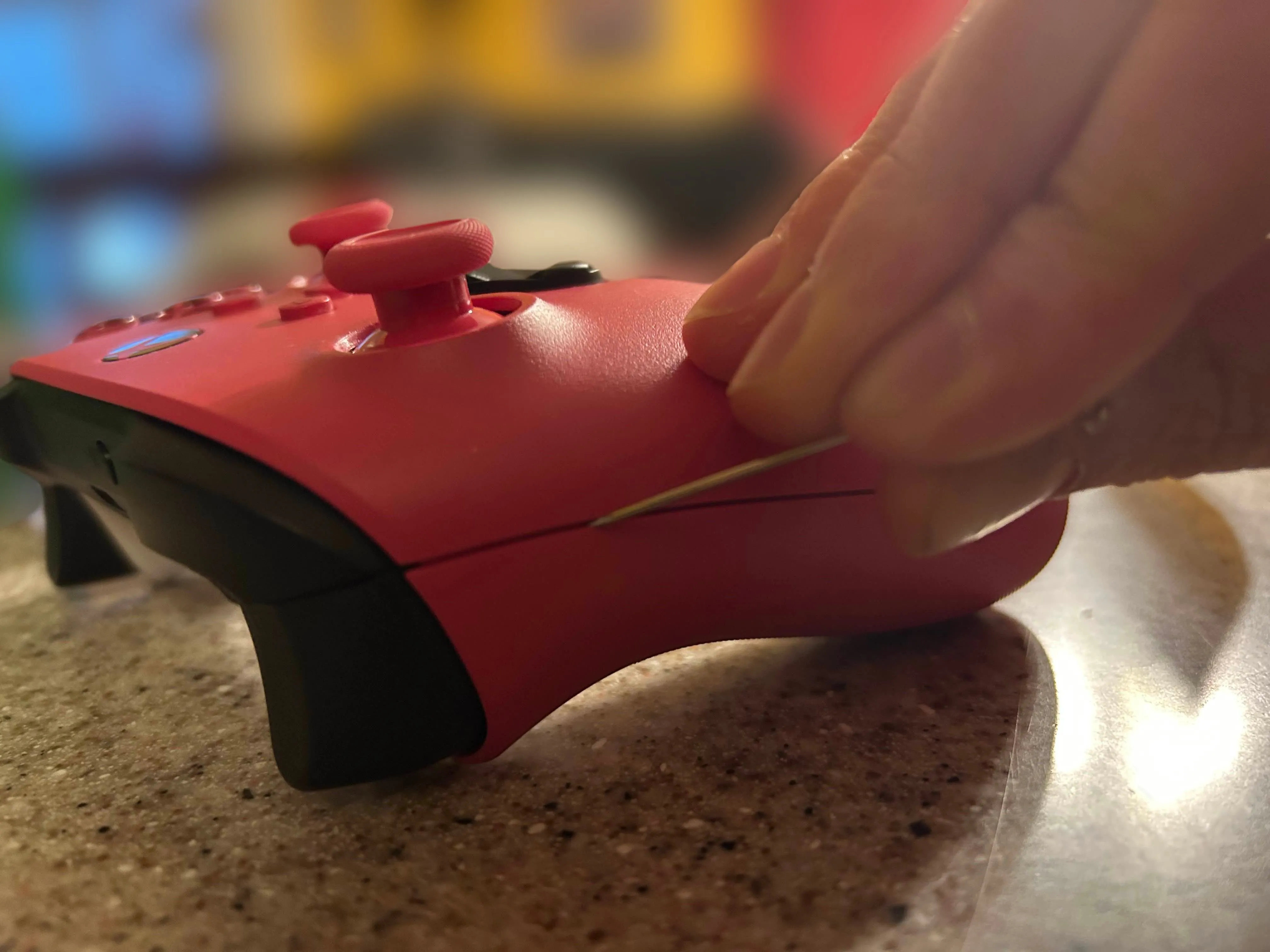 Dùng dụng cụ kim loại làm sạch bụi bẩn và da chết ở đường nối của tay cầm Xbox màu hồng.