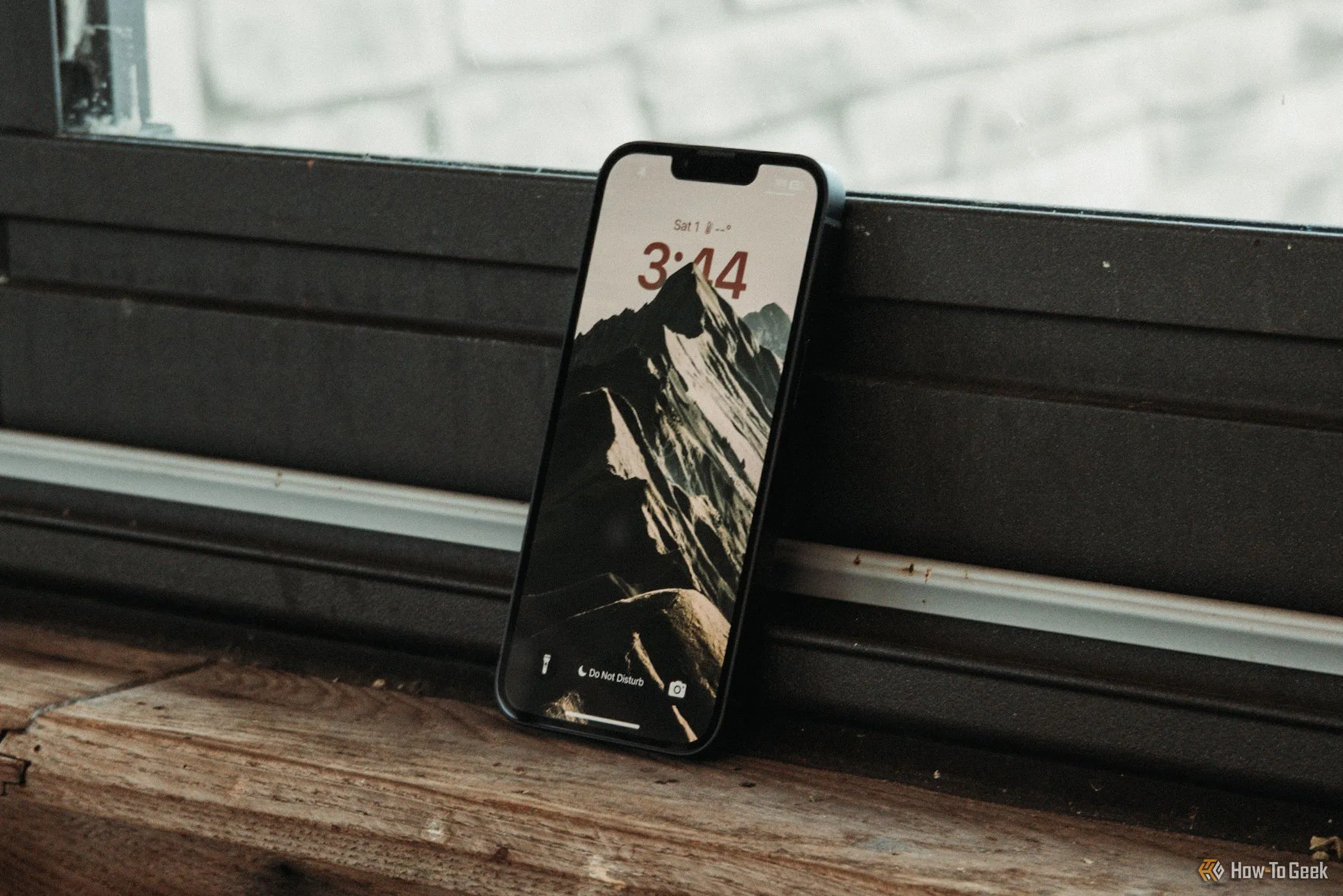 Màn hình khóa của iPhone 16e được đặt nghiêng trên bệ cửa sổ, thể hiện giao diện người dùng iOS và thiết kế màn hình 6.1 inch