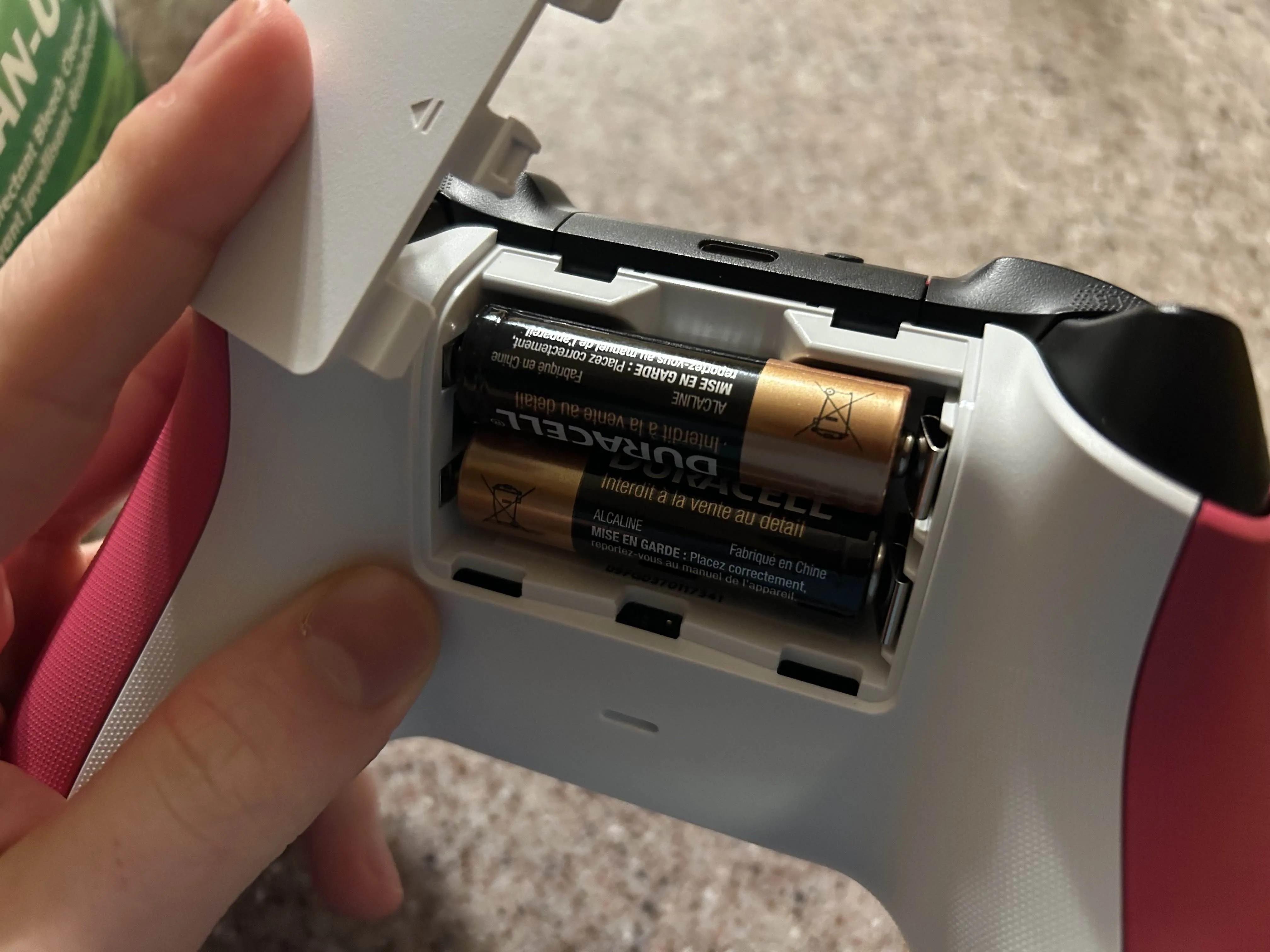 Mở ngăn chứa pin của tay cầm Xbox màu hồng, chuẩn bị vệ sinh khoang pin.