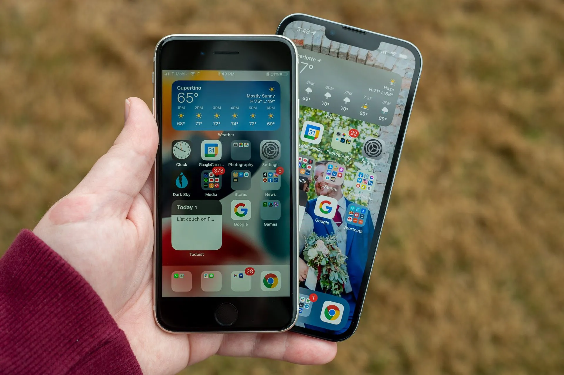 Một bàn tay đang cầm hai chiếc điện thoại iPhone SE (2022) và iPhone 13 Pro.