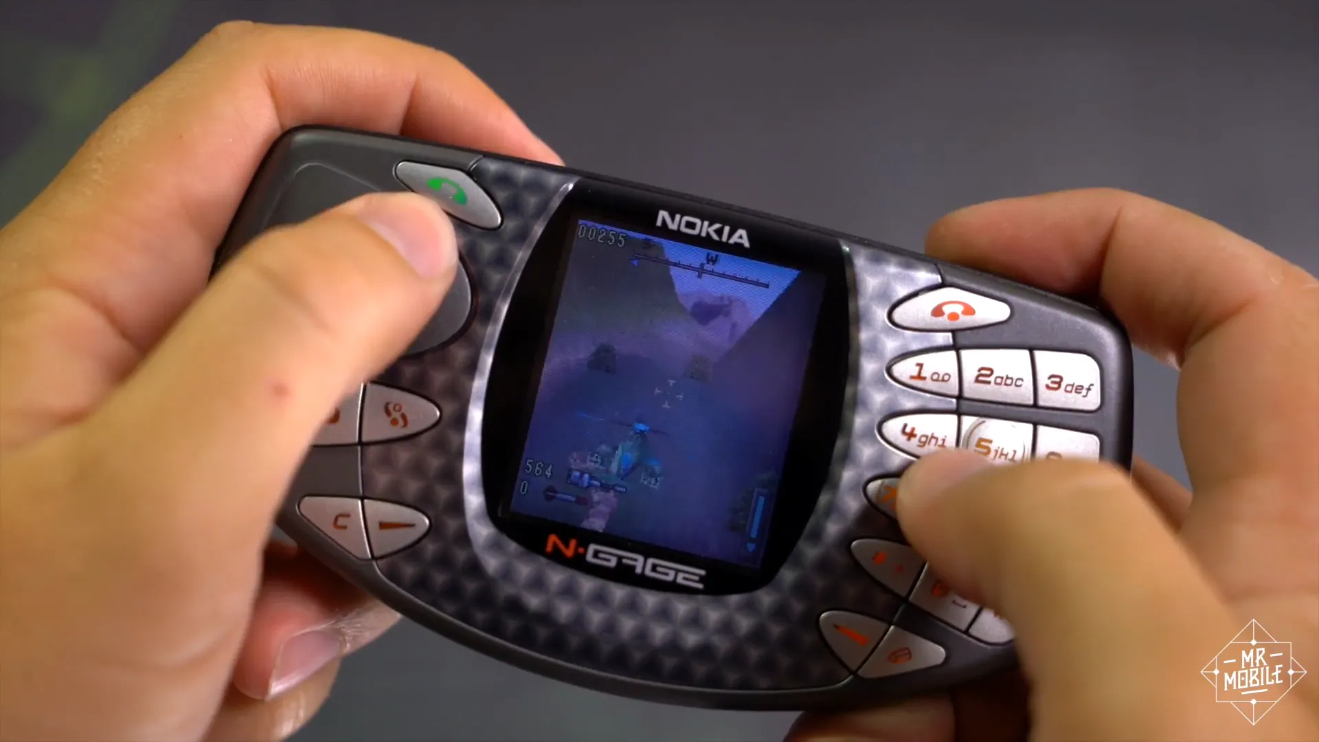 MrMobile (Michael Fisher) đang chơi game trên chiếc Nokia N-Gage, minh họa cách người dùng phải cầm ngang điện thoại để chơi game hoặc nghe gọi vì thiết kế đặc trưng của máy.