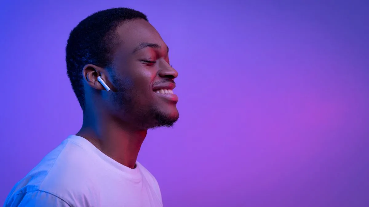 Người đàn ông với vẻ mặt thư giãn đang đeo tai nghe Apple AirPods, minh họa việc sử dụng âm thanh để thiền định hoặc thư giãn mà không cần nhìn vào màn hình điện thoại.