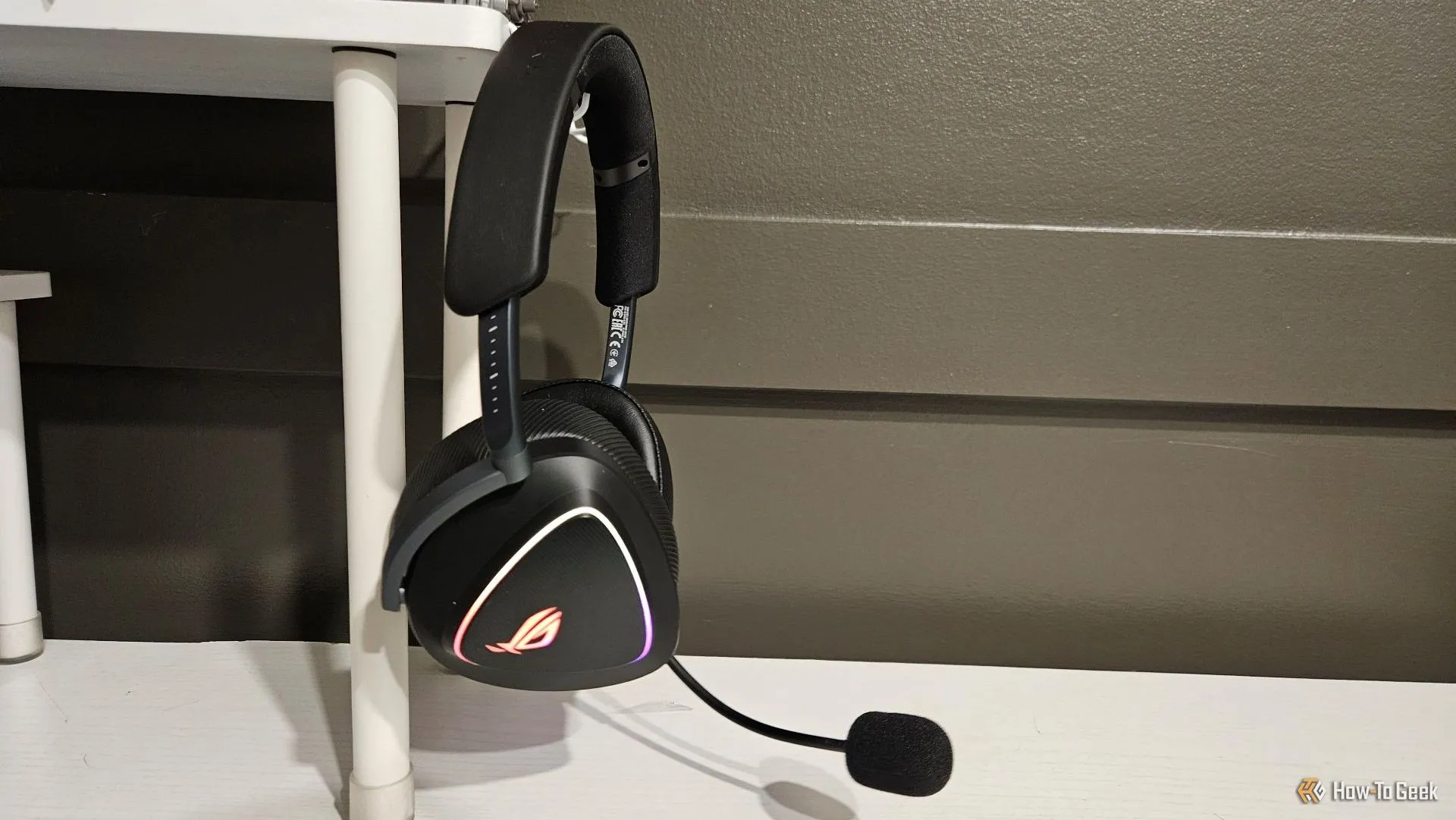 Tai nghe ASUS ROG Delta II màu đen được treo trên giá đỡ tai nghe ở cạnh bàn làm việc, thể hiện vẻ ngoài hiện đại và gọn gàng của sản phẩm.