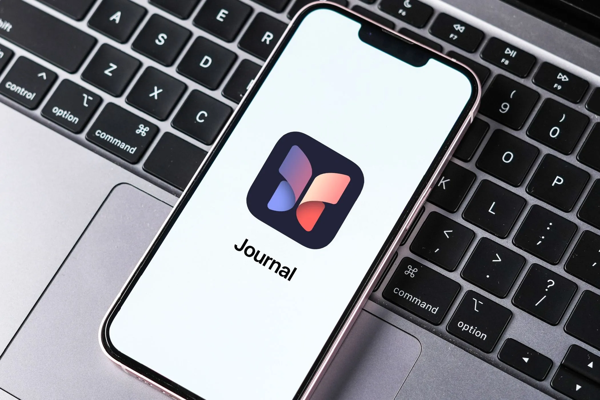 Ứng dụng Journal của Apple hiển thị trên màn hình iPhone, đặt trên bàn phím MacBook, minh họa công cụ nhật ký kỹ thuật số của Apple.