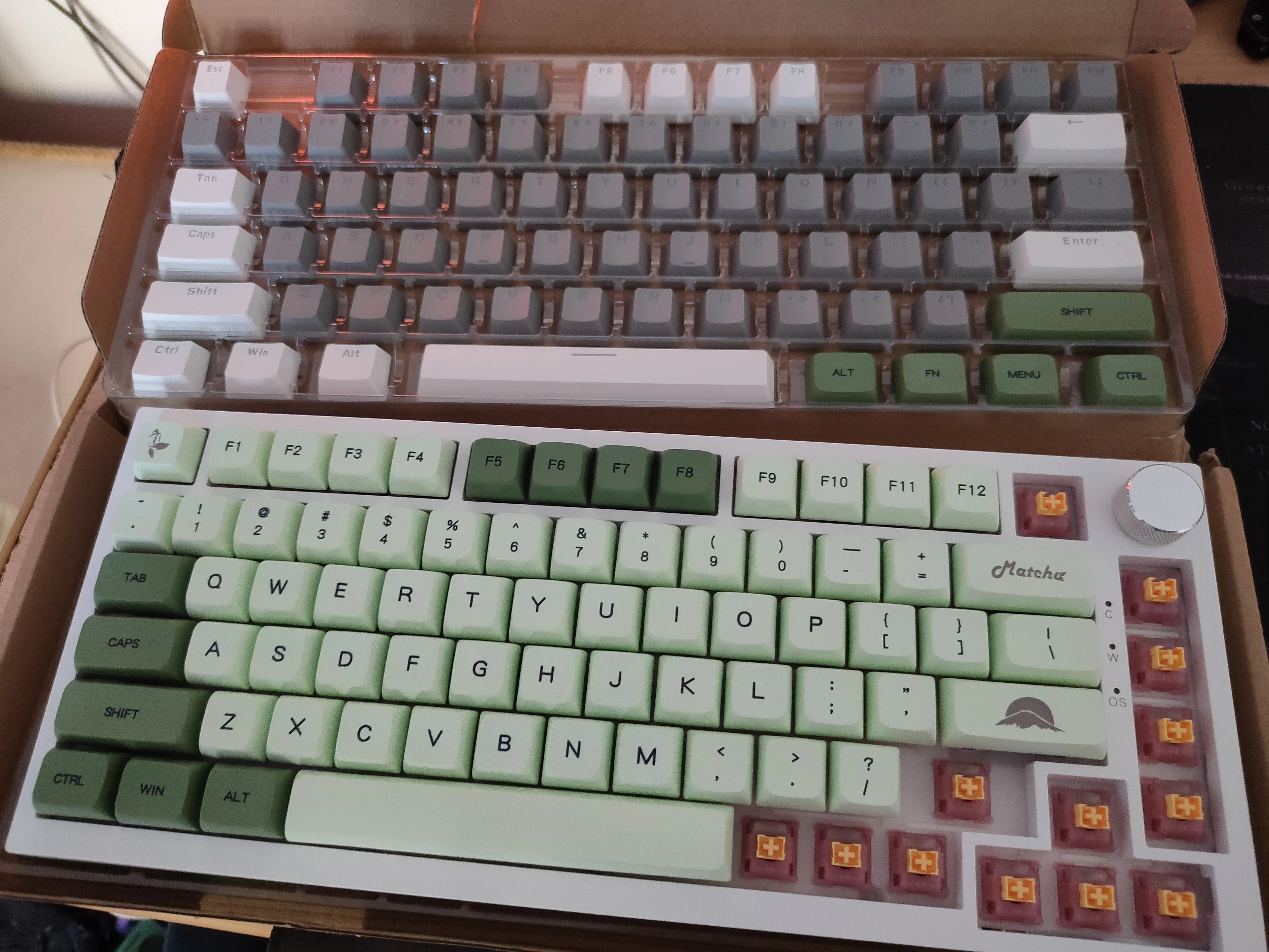 Bàn phím Ajazz AK820 với keycaps tùy chỉnh màu xanh lá cây và keycaps gốc phía trên, cho thấy việc thay thế keycaps có thể làm mất ký hiệu phím media.