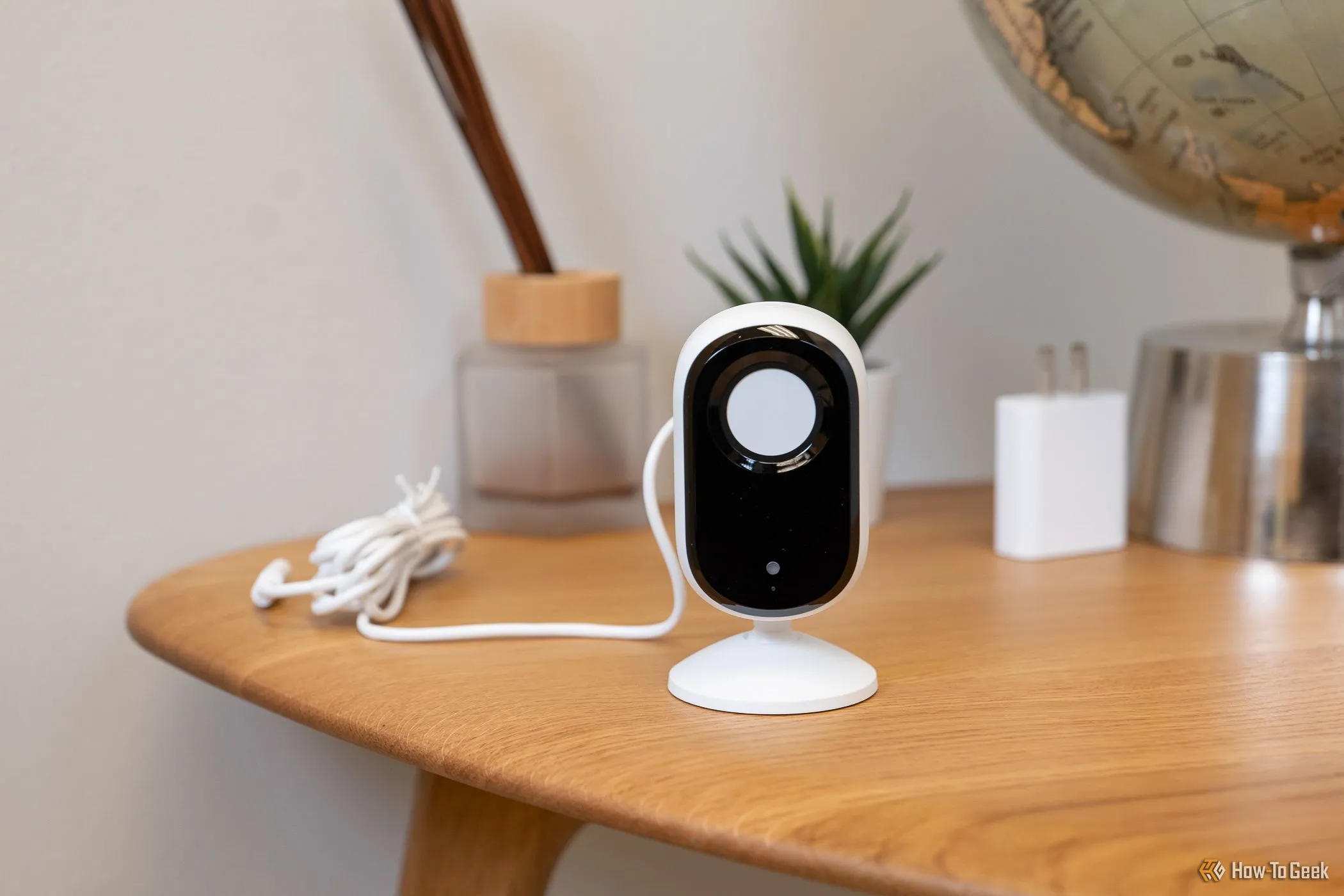 Camera an ninh trong nhà Arlo Essential Indoor Cam 2K đặt trên bàn, màn che riêng tư đang đóng để bảo vệ quyền riêng tư.