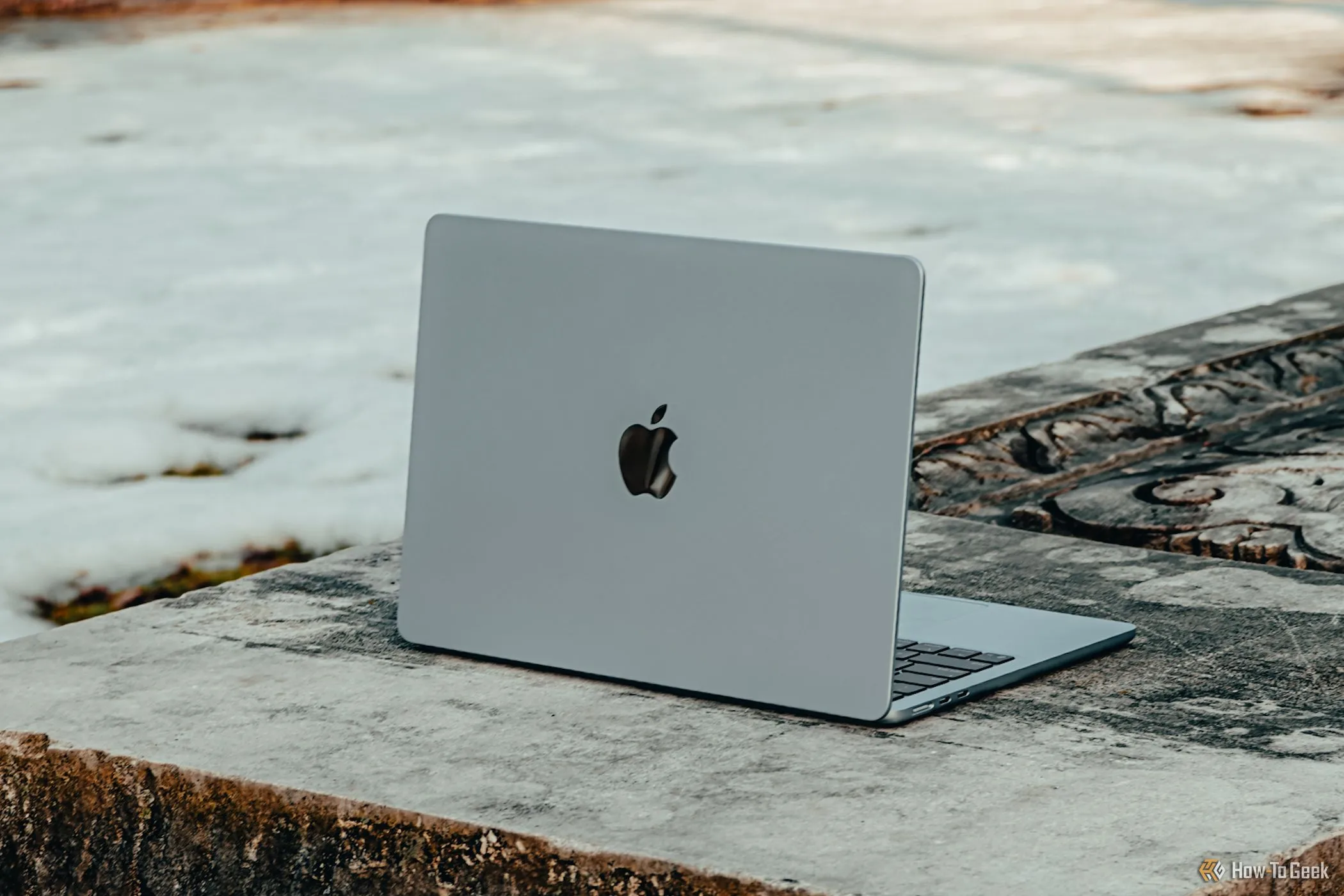 Chiếc MacBook Air M4 màu xanh lam nằm trên ghế đá, nhìn nghiêng, thể hiện thiết kế sang trọng nhưng khó sửa chữa theo đánh giá của iFixit.