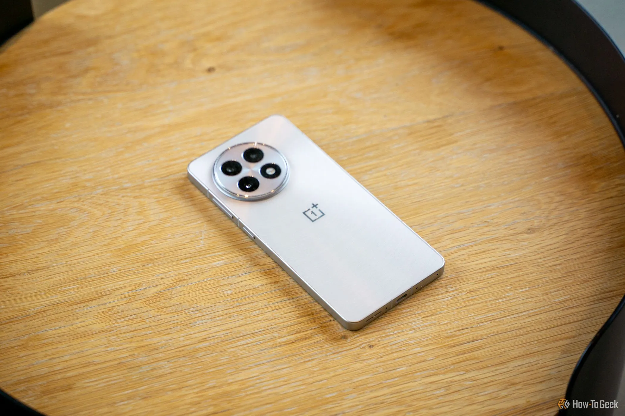 Điện thoại OnePlus 13R với cụm ba camera sau cao cấp, nằm trên bàn gỗ.