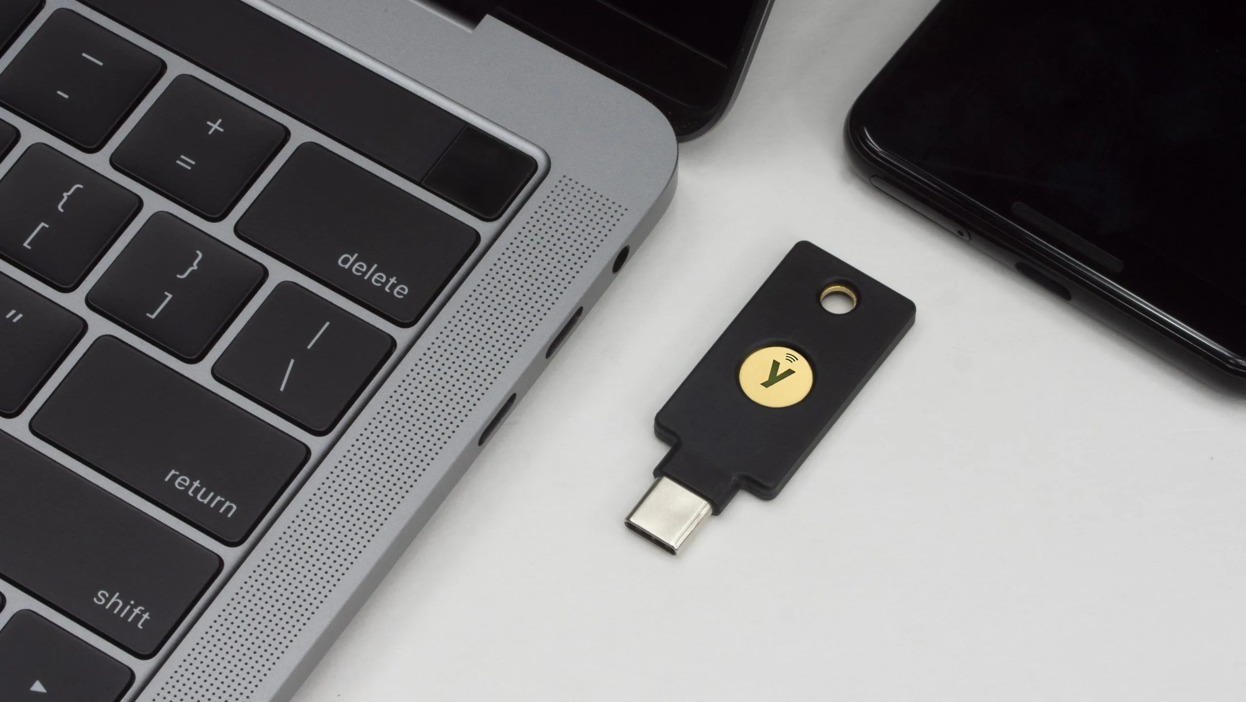 Khóa bảo mật YubiKey 5C NFC đặt cạnh MacBook và điện thoại Android, minh họa khả năng tương thích đa thiết bị