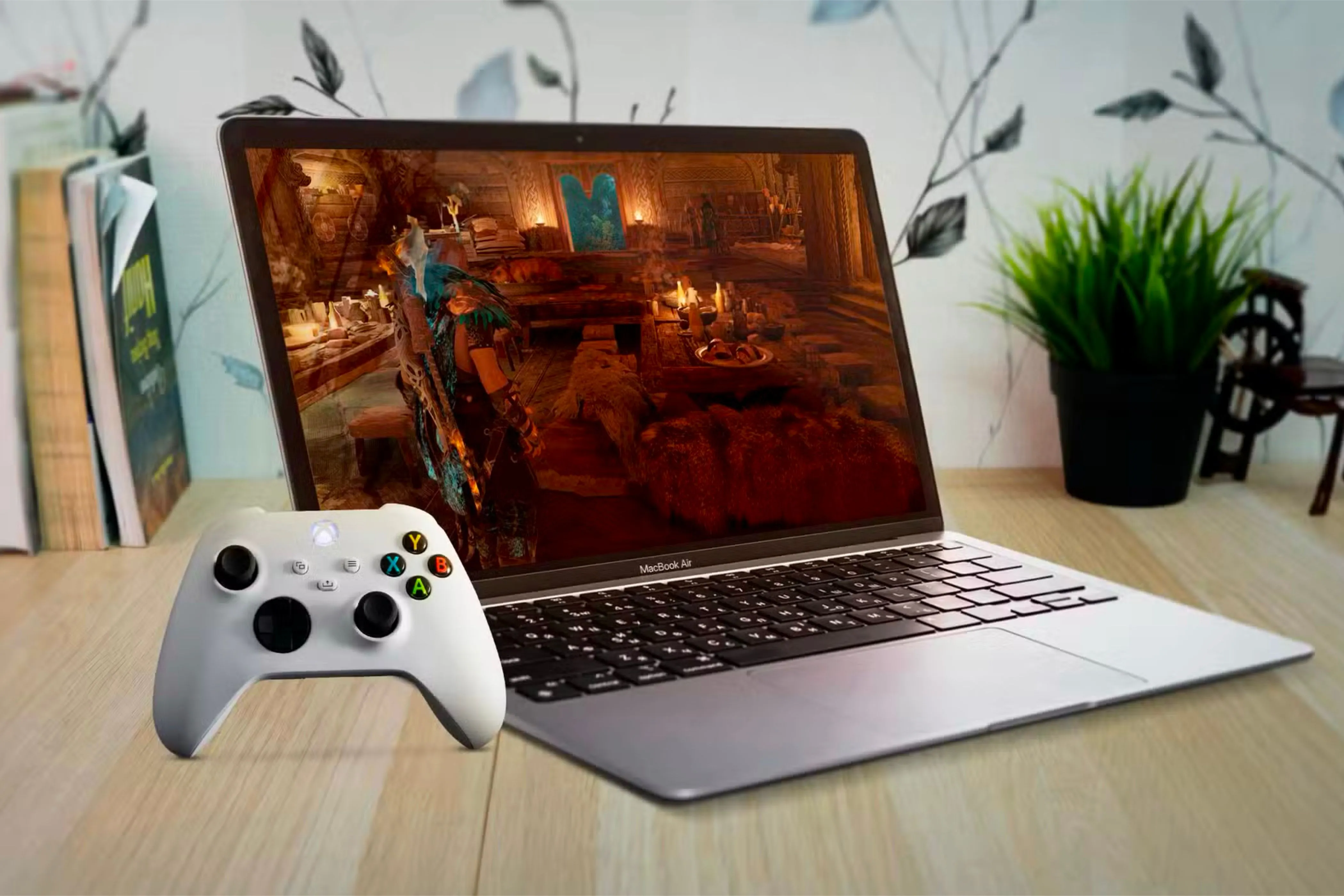 Một chiếc MacBook Air đặt dưới bàn gỗ với màn hình hiển thị game và tay cầm Xbox bên trái