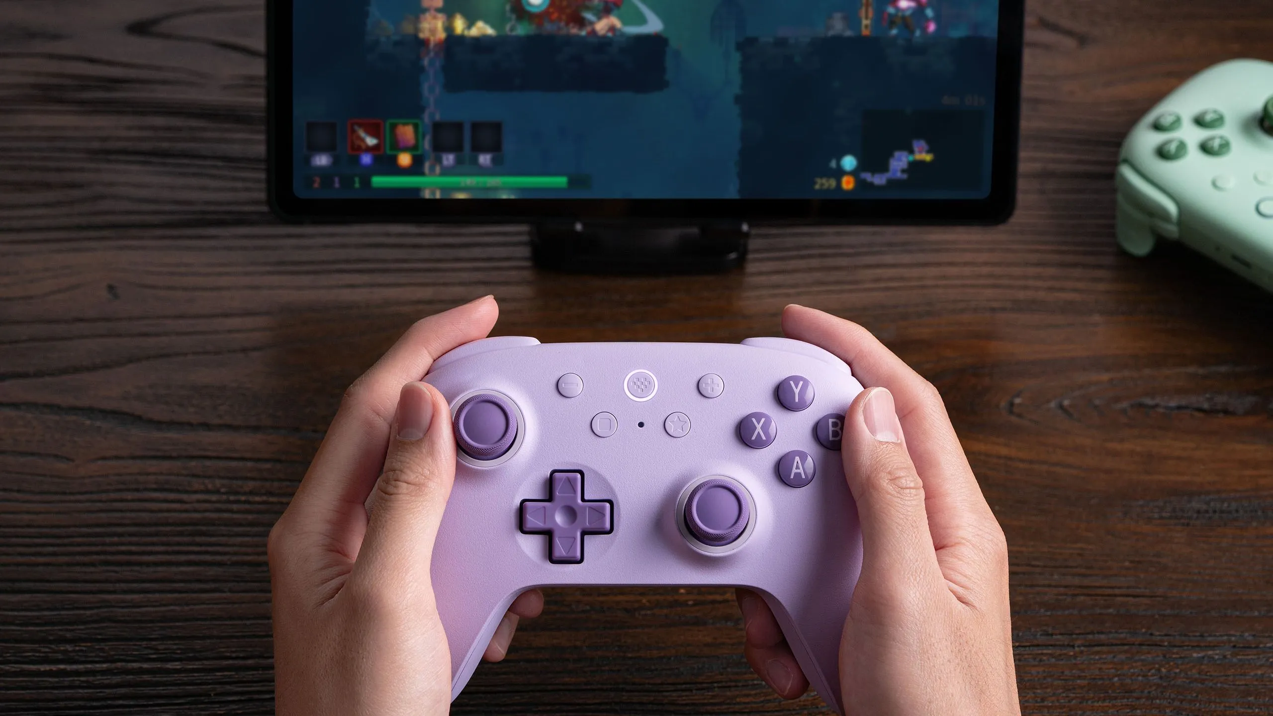 Một người đang cầm tay cầm 8BitDo Ultimate 2C Wireless và chơi Dead Cells trên máy tính bảng.