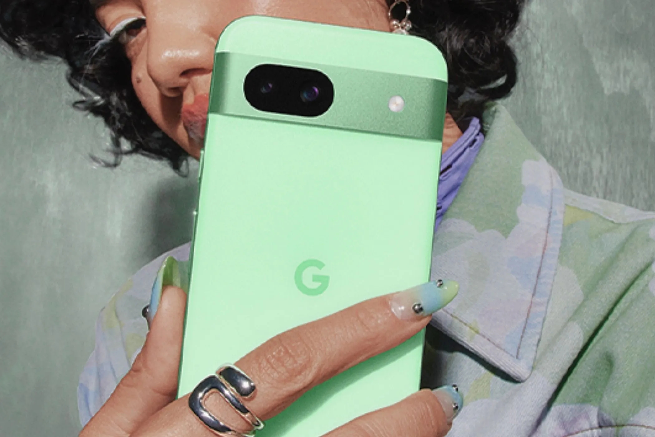 Một phụ nữ đang cầm chiếc Google Pixel 8a màu xanh Aloe, cho thấy thiết kế và màu sắc của điện thoại.