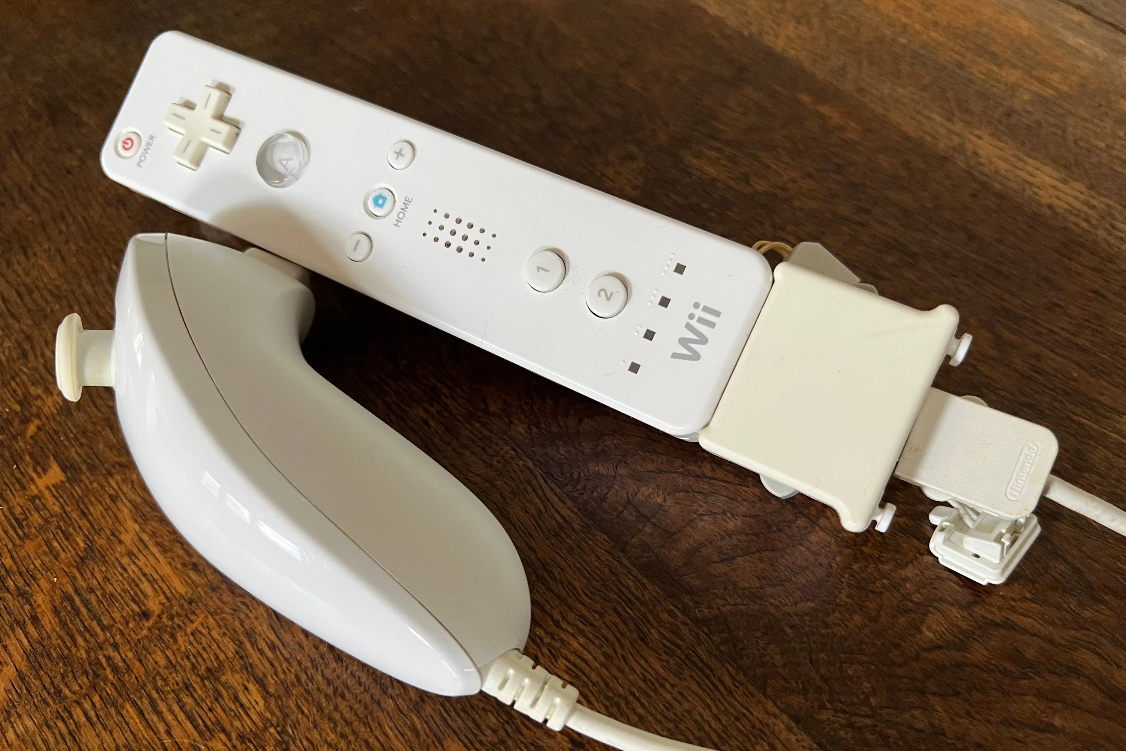 Một tay cầm Wii Remote màu vàng nhạt, đi kèm Wii Motion Plus và Wii Nunchuk, cho thấy sự đa năng của thiết bị