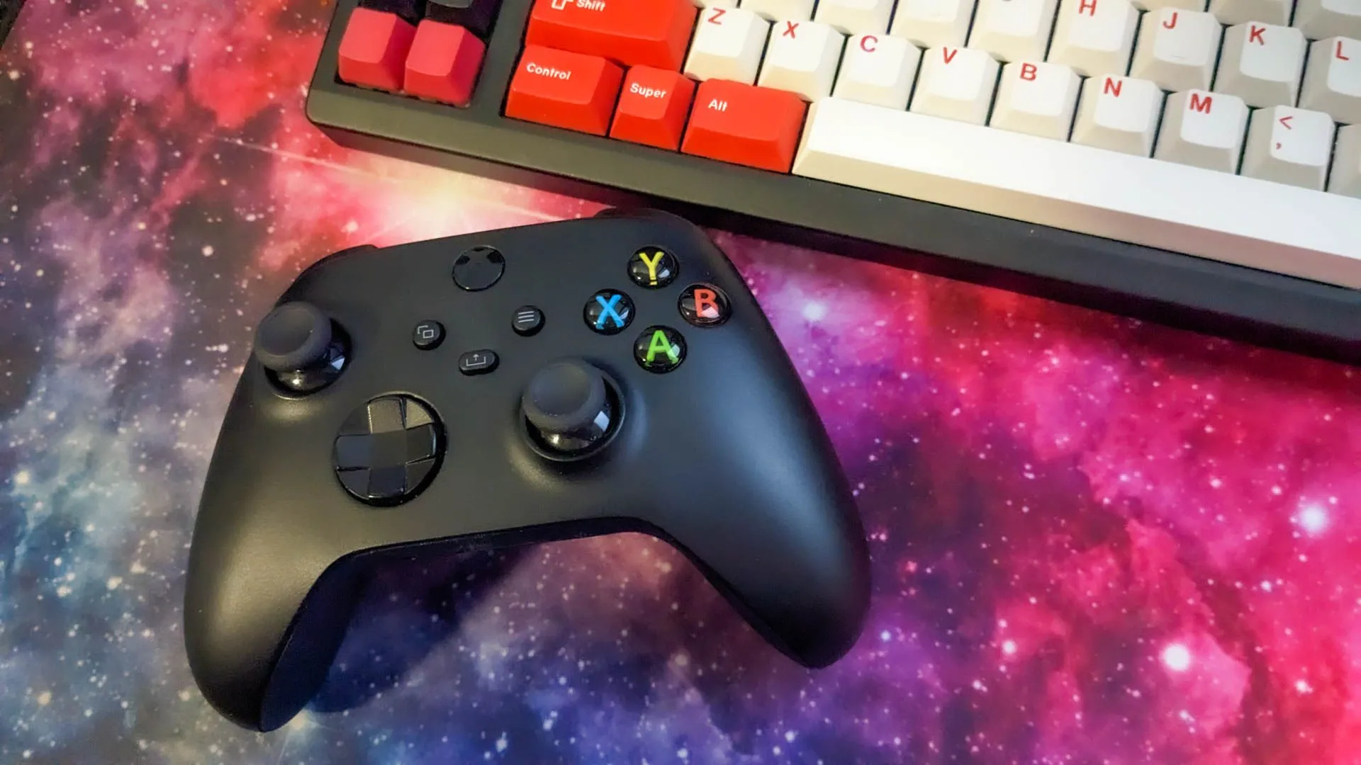 Một tay cầm Xbox đặt cạnh bàn phím cơ và chuột gaming trên bàn di chuột không gian, minh họa sự đa dạng về thiết bị điều khiển khi chơi game trên PC.