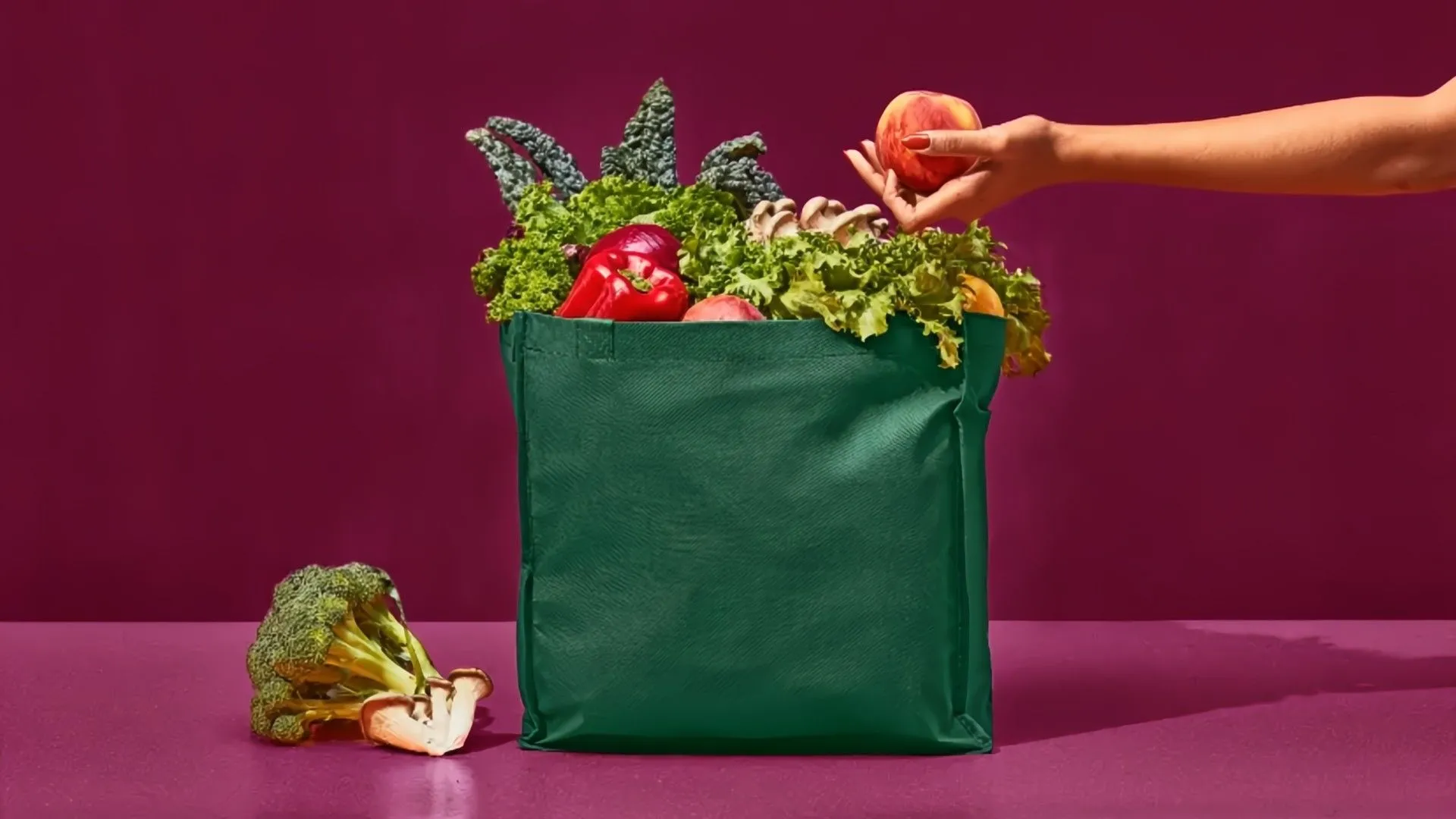 Người đang đặt trái cây vào túi mua sắm màu xanh lá, minh họa cho dịch vụ giao hàng Instacart