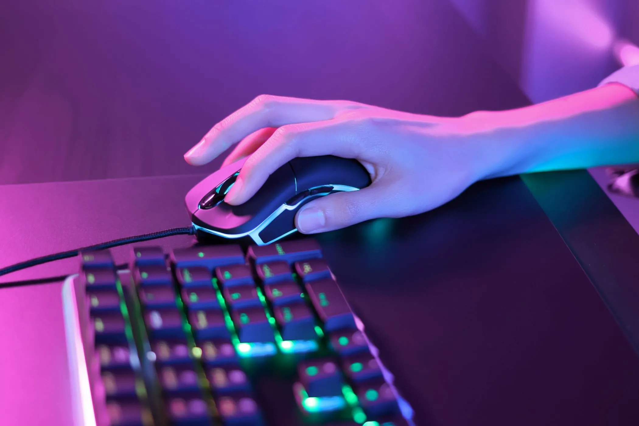 Người dùng đang sử dụng chuột gaming dưới ánh đèn neon hồng cạnh bàn phím RGB