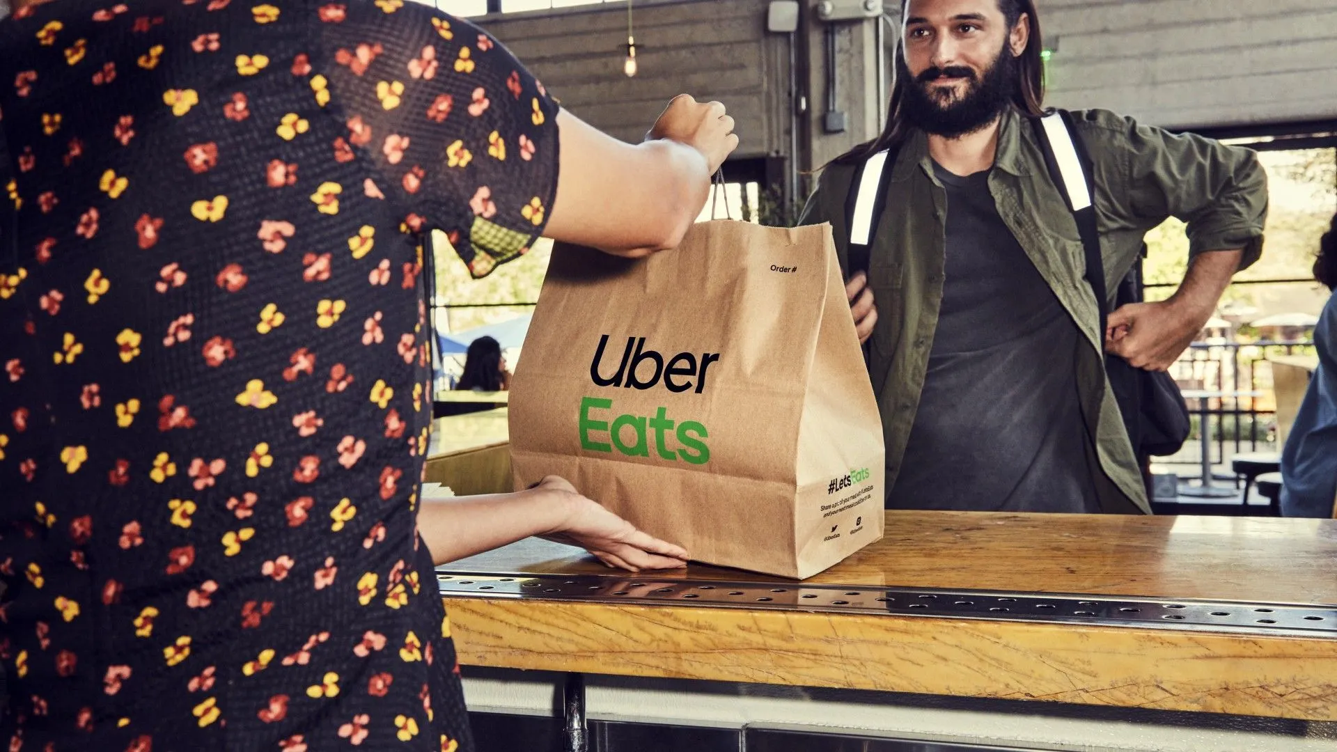 Người giao hàng đang nhận túi đồ ăn Uber Eats từ nhà hàng, minh họa công việc giao hàng kiếm thêm thu nhập