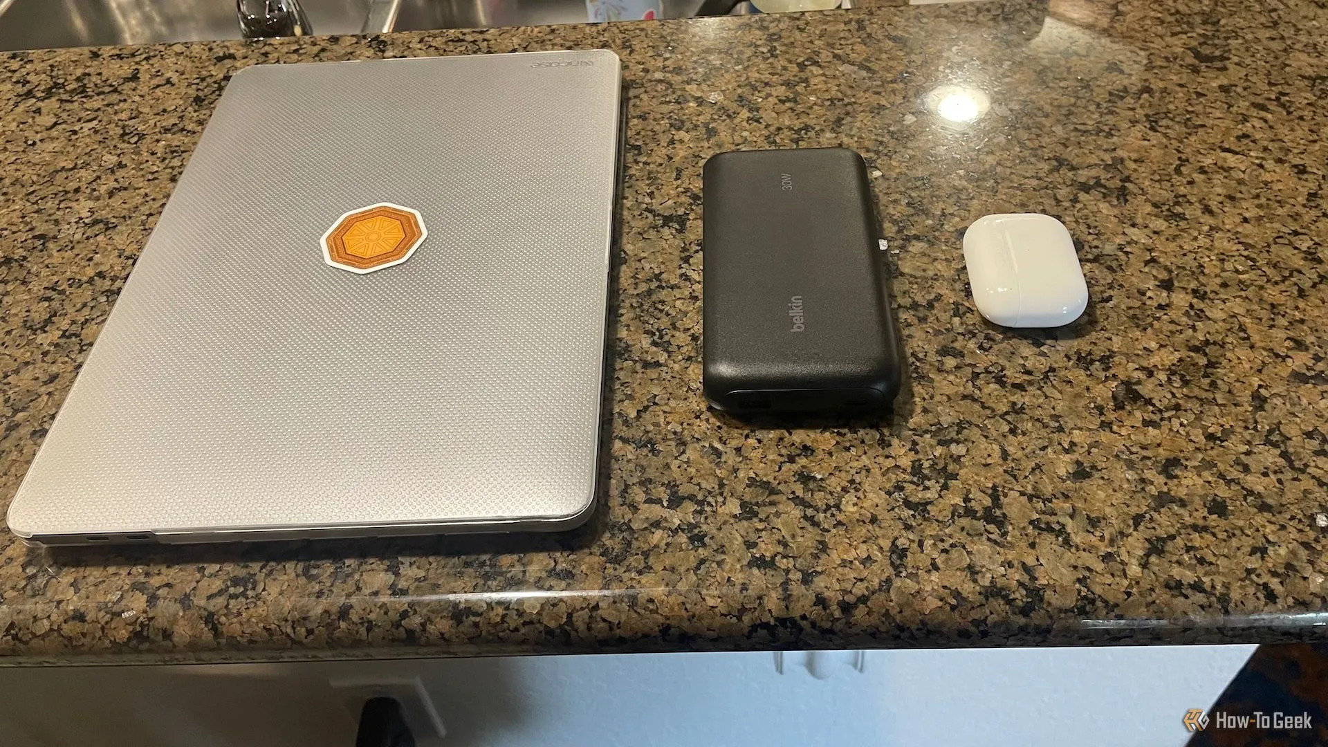 Pin sạc dự phòng Belkin BoostCharge Power Bank 20K đặt cạnh MacBook Pro và hộp sạc AirPods, thể hiện kích thước và khả năng sạc thiết bị lớn hơn.