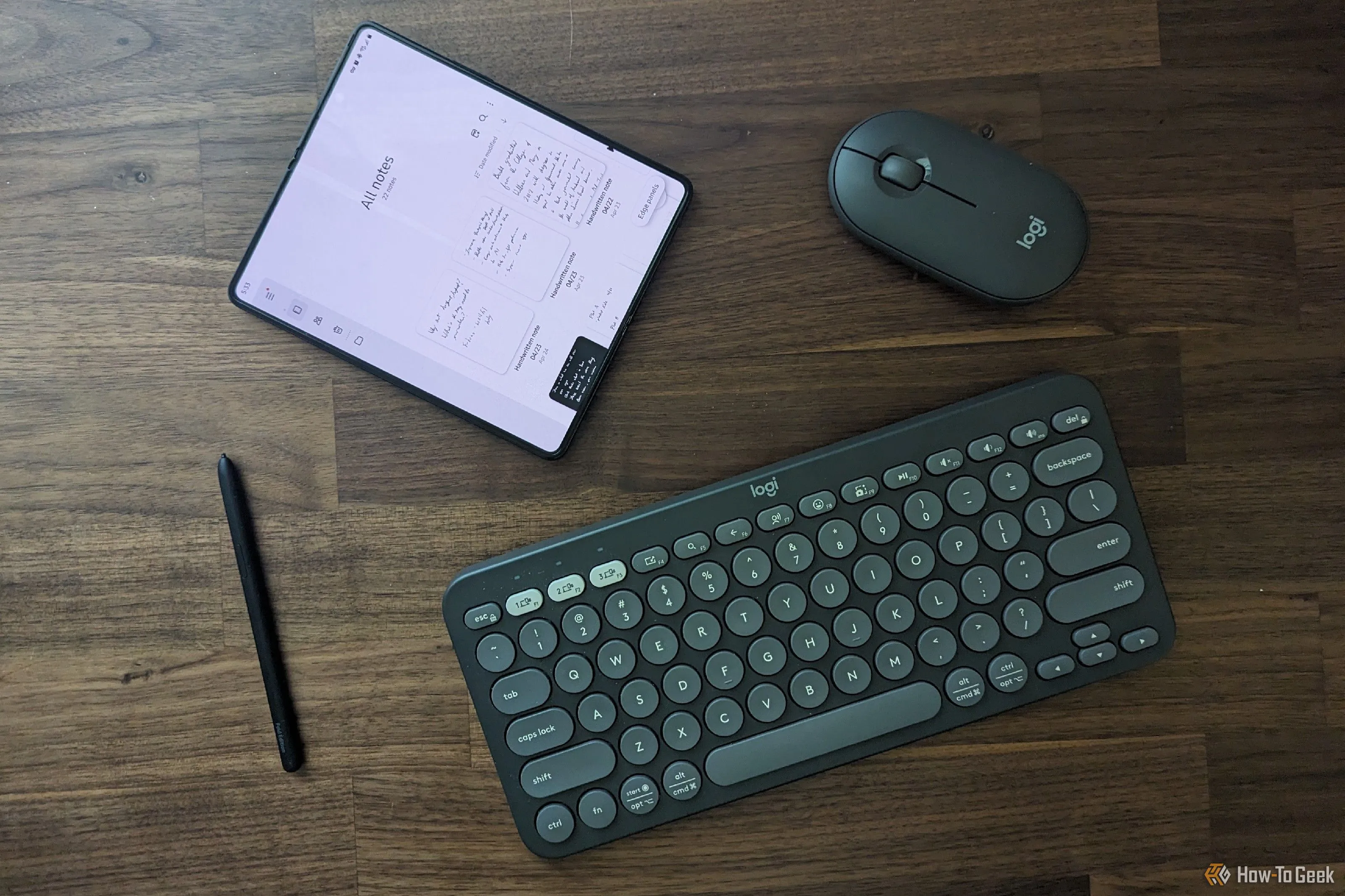 Samsung Galaxy Z Fold 5 màu đen gập mở, đặt trên bàn làm việc cùng với bút S Pen, bàn phím Bluetooth và chuột không dây.