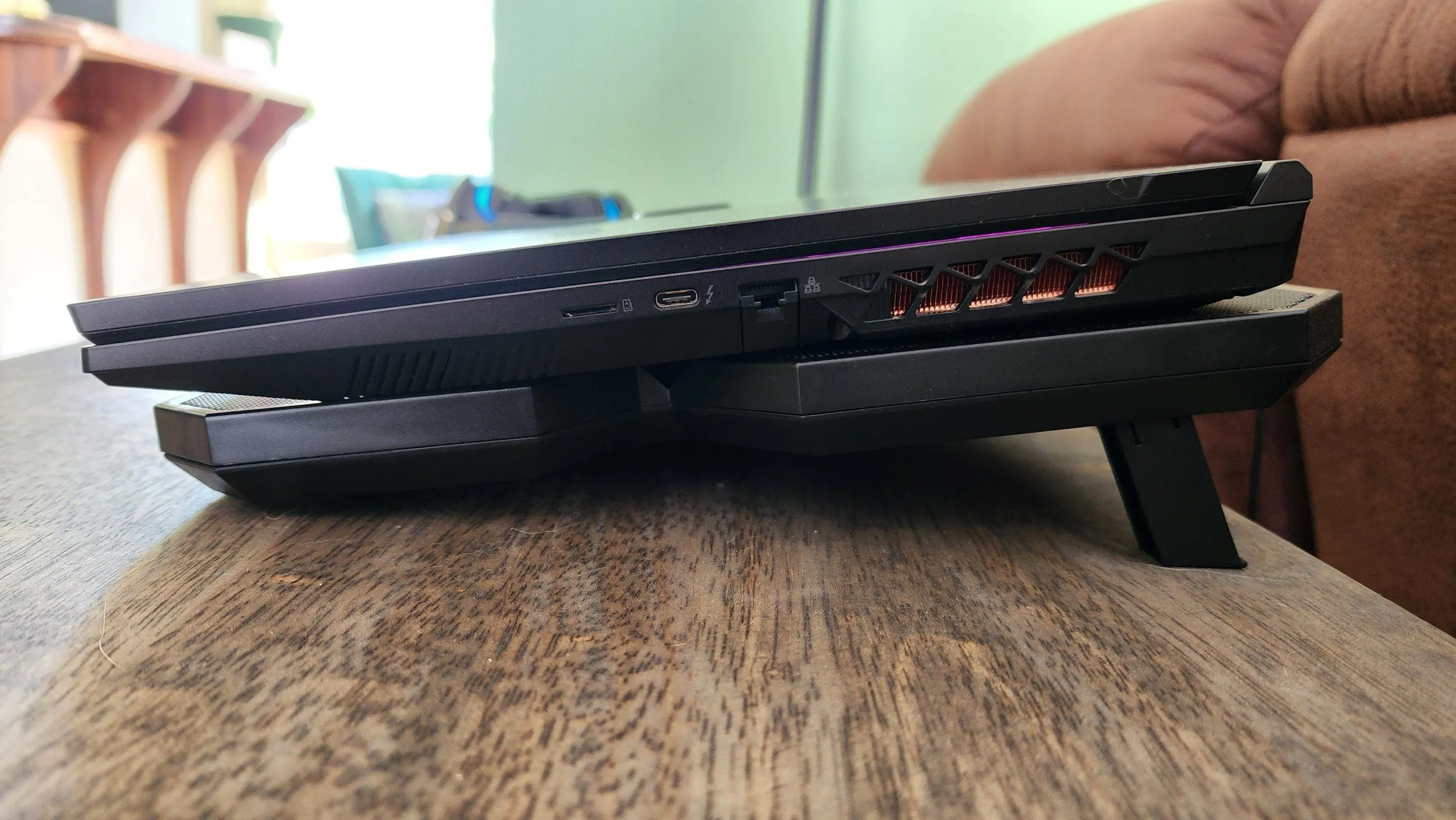 Laptop gaming đặt trên đế tản nhiệt chủ động nhìn từ cạnh bên, cho thấy khe thoát khí và khả năng tăng luồng gió mát.