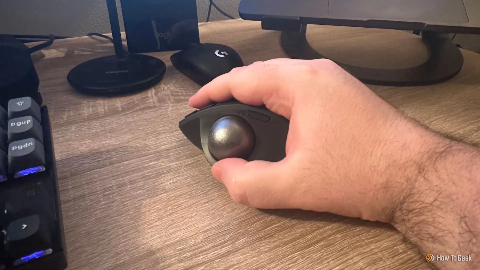 Bàn tay phải cầm chuột Logitech MX Ergo S, cho thấy thiết kế công thái học và vị trí đặt ngón cái trên bi lăn