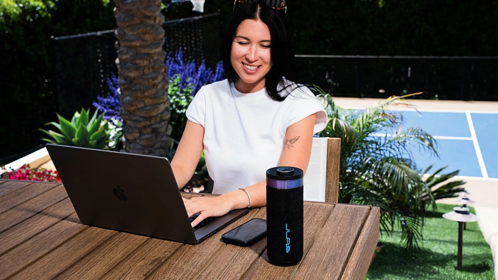 Loa JLab Go Party trên bàn cạnh một người phụ nữ sử dụng máy tính