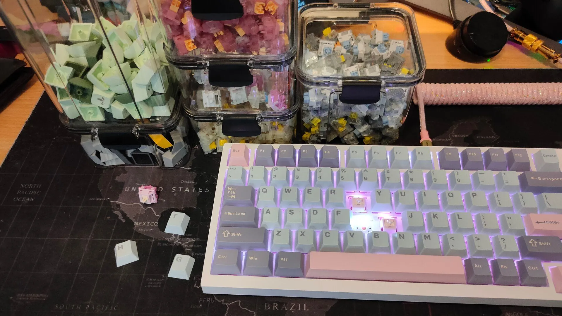 Một bàn phím cơ tùy chỉnh với các keycap và switch đặt trong hộp trong suốt ở hậu cảnh, thể hiện sự đam mê sưu tầm phụ kiện bàn phím.