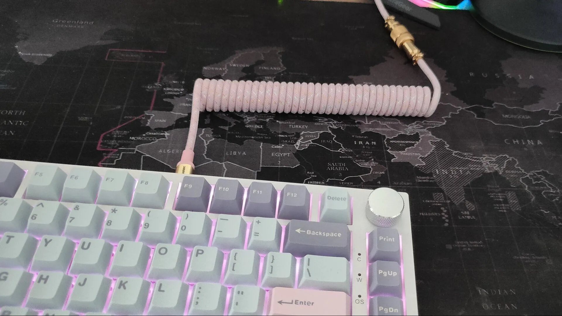 Một sợi cáp bàn phím cuộn màu hồng được cắm vào một bàn phím màu trắng với keycap màu xanh nhạt và tím.