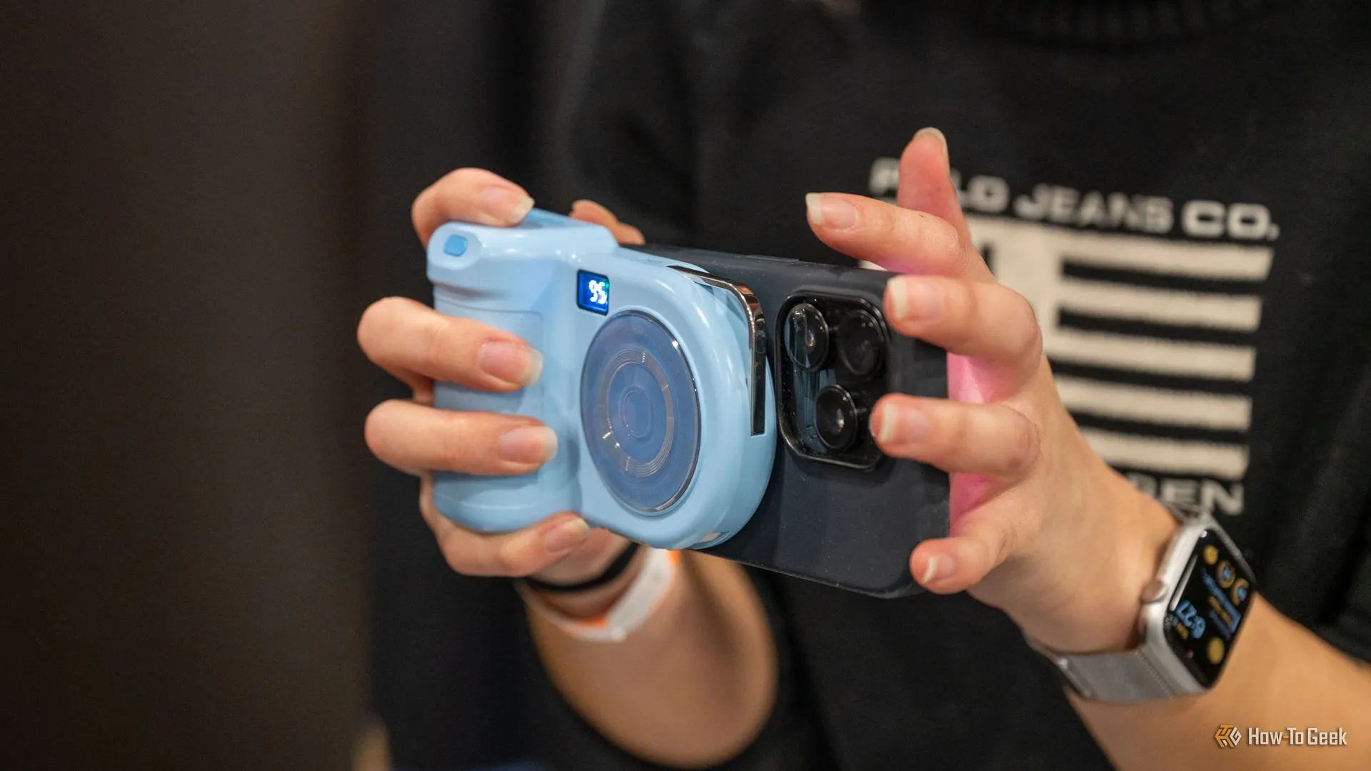 Người dùng cầm iPhone gắn sạc dự phòng MagSafe Belkin Stage PowerGrip hình máy ảnh, minh họa kích thước cồng kềnh.