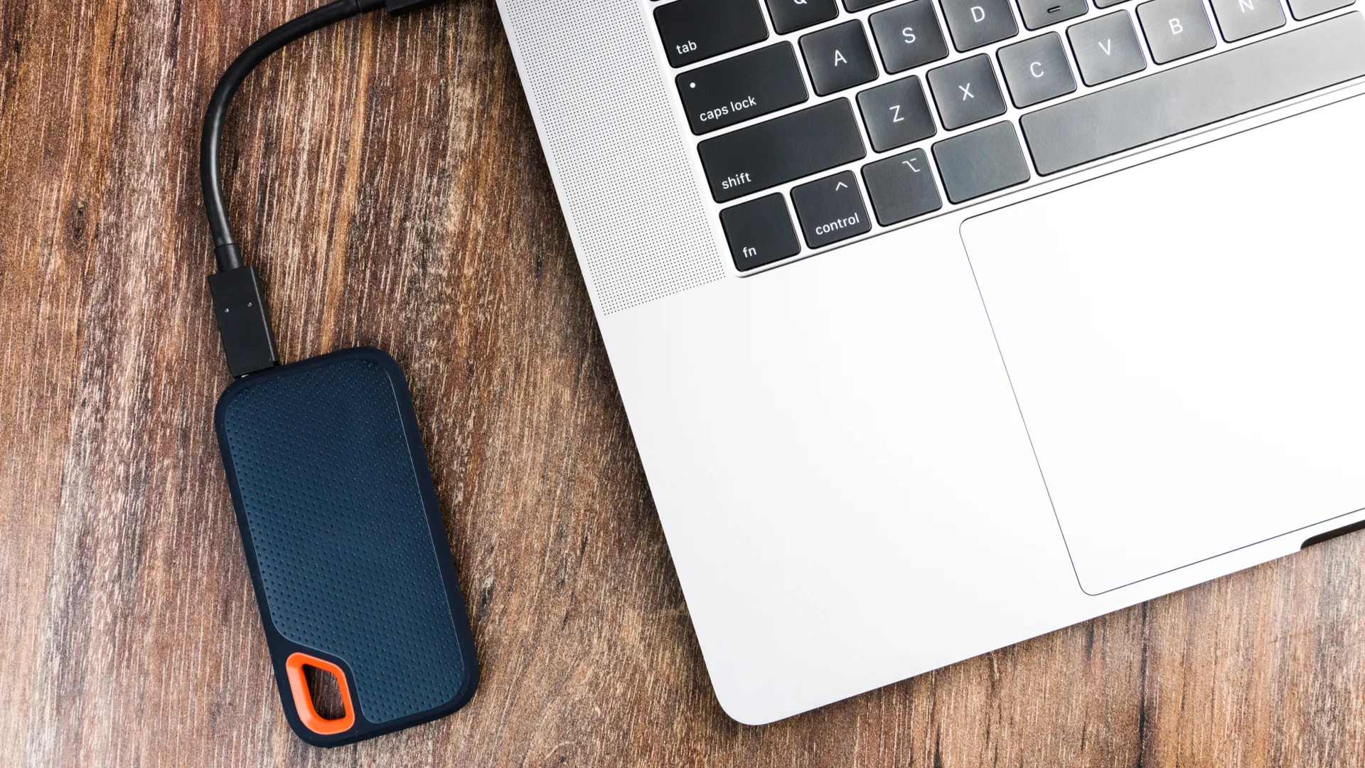 Ổ đĩa SSD gắn ngoài được kết nối với máy tính Mac trên nền gỗ, thể hiện giải pháp sao lưu Time Machine hiệu quả.